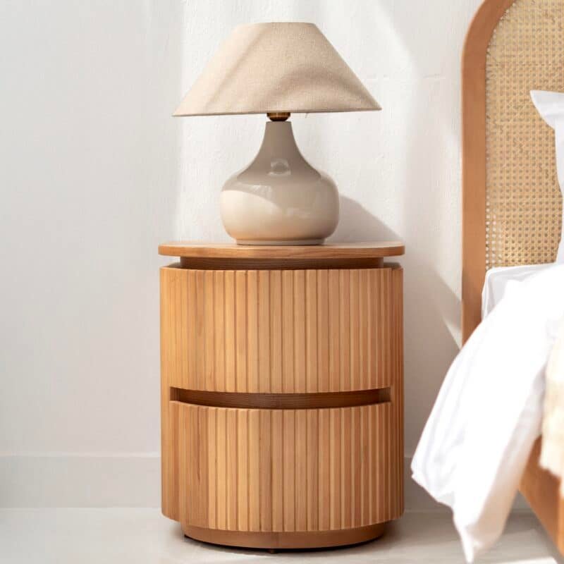 Round wooden bedside table with lamp beside a bed