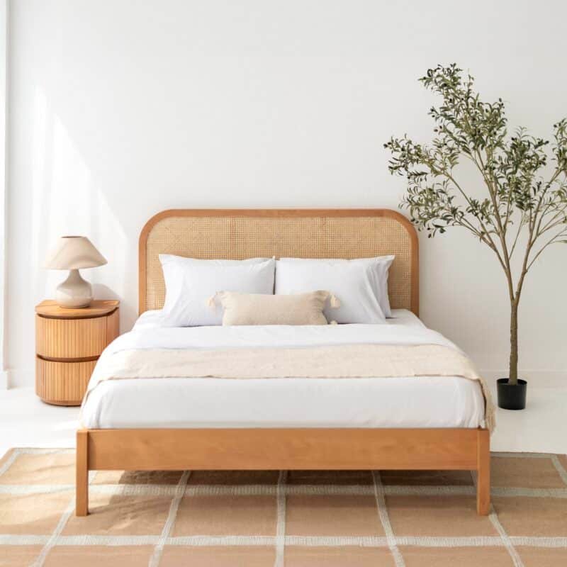 Wooden bed with woven cane headboard and round bedside table in a styled bedroom