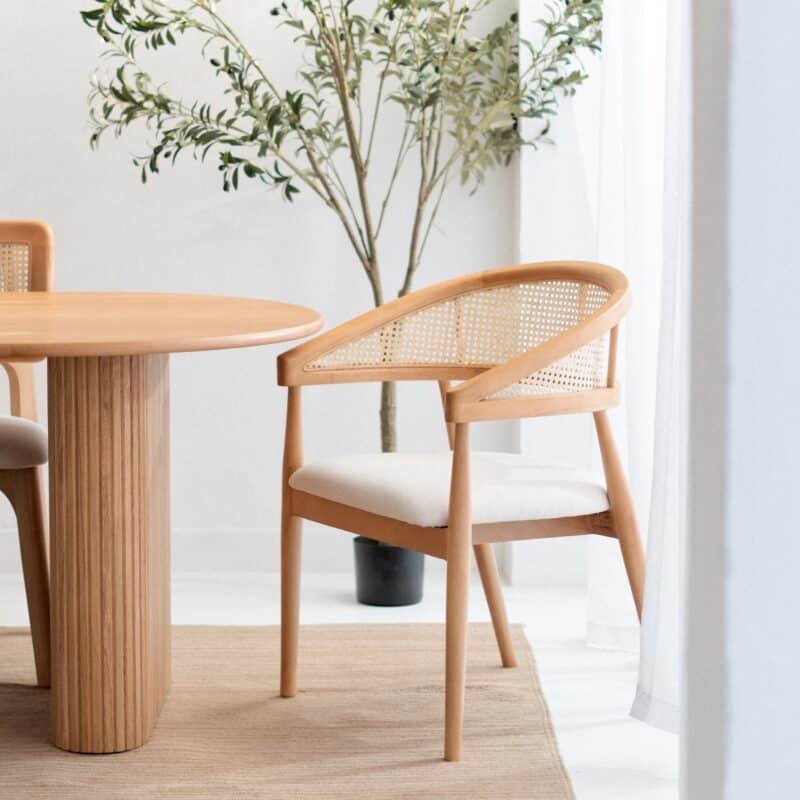 Wooden dining chair beside a round wooden table with plant in background